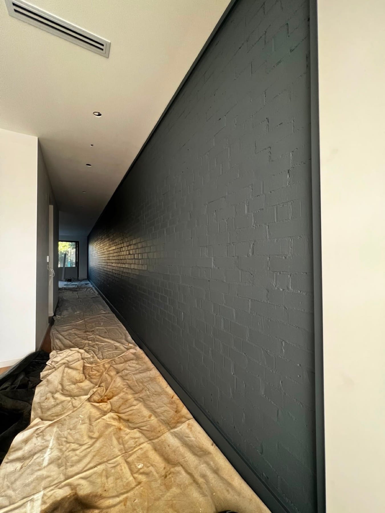 Exposed brick wall painted deep charcoal as a hallway feature, after