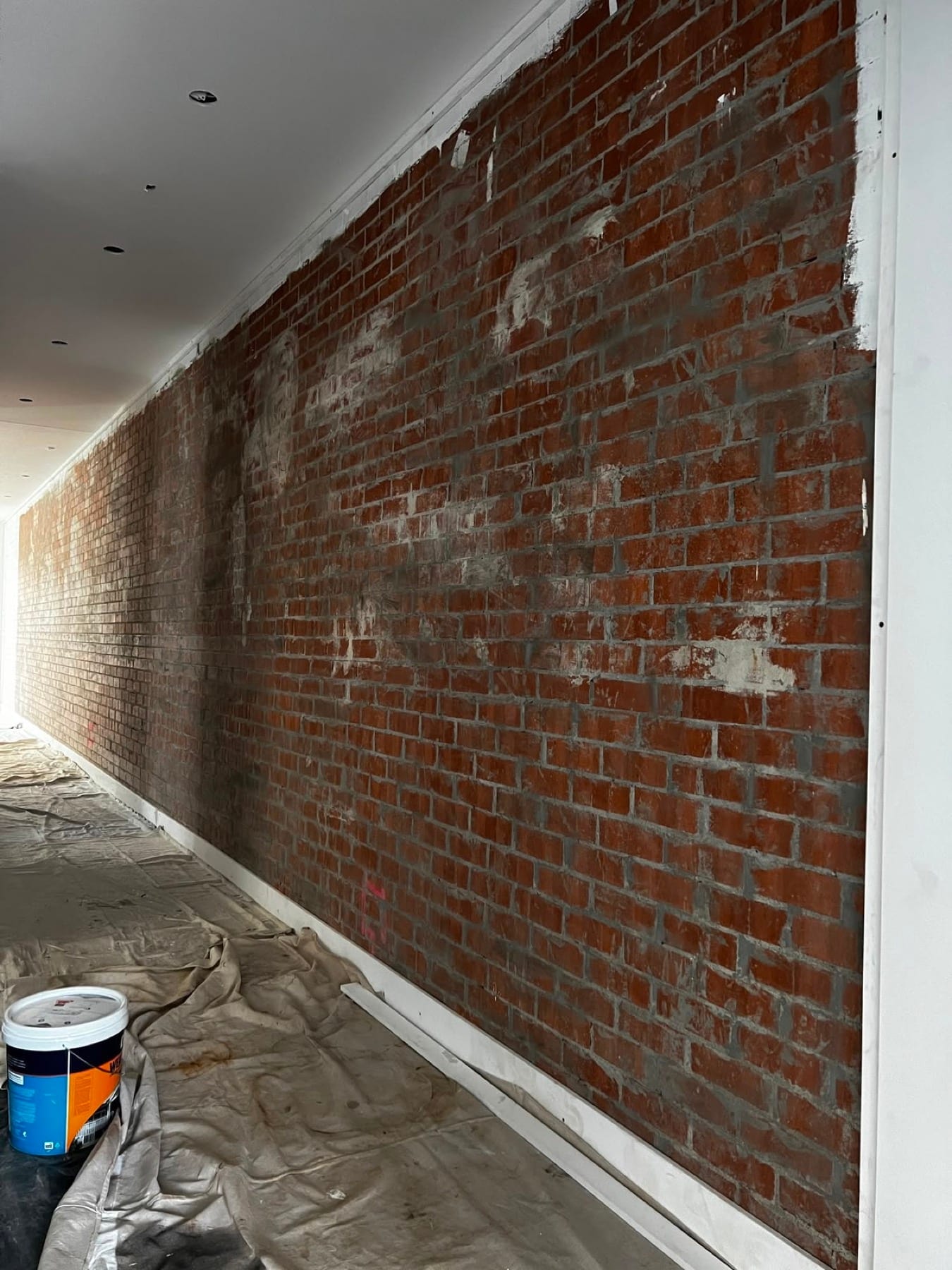 Exposed brick wall painted deep charcoal as a hallway feature, before